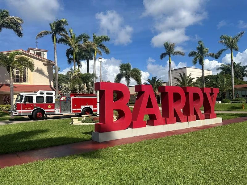 A large red "BARRY" sign is displayed on a grassy area with a fire truck parked nearby and palm trees in the background.