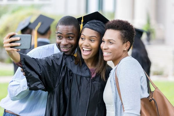 Three people are taking a happy selfie at a graduation ceremony.